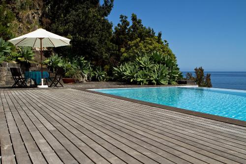 a swimming pool with an umbrella on a wooden deck at Casa do Lado in Povoação