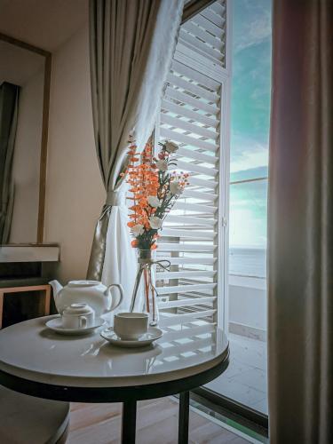 a table with two cups and a vase with flowers at TMS Pullman Quy Nhơn Căn Hộ - Xuân Phương Apartment in Quy Nhon