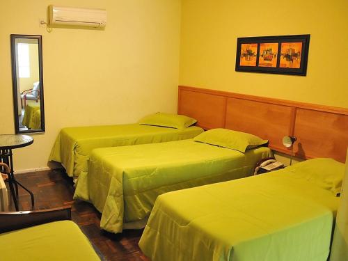 a room with three beds with green sheets at Hotel Uruguay Brasil in Rivera