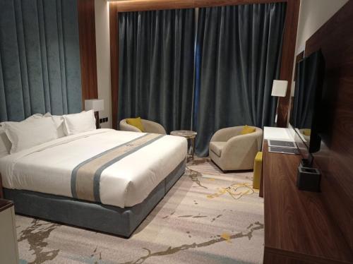 um quarto com uma cama, uma televisão e uma cadeira em Rosa Grand Hotel em Riade