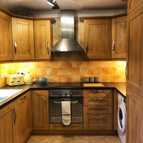 uma cozinha com armários de madeira e um forno com placa de fogão em The Rose Cottage em Wisborough Green