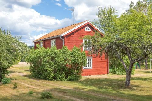 una casa roja con un árbol delante en Cozy cottage with proximity to lake with jetty en Vimmerby
