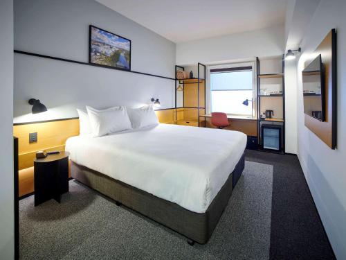 um quarto com uma grande cama branca e uma secretária em ibis Hamilton Tainui em Hamilton