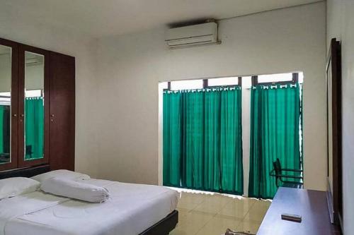una camera da letto con tende verdi, un letto e una scrivania di Graha HT Sumantri Mitra RedDoorz a Tasikmalaya