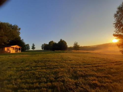 einen Sonnenuntergang auf einem Feld mit einem Haus im Hintergrund in der Unterkunft Chatka na Wzgórzu, Staw z możliwością łowienia ryb, Cisza, Spokój in Barczewo