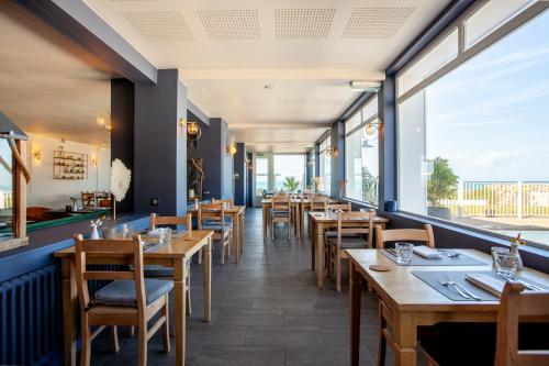 a restaurant with wooden tables and chairs and large windows at Hôtel des Isles in Barneville-Carteret