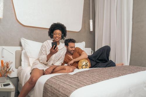 a man and woman sitting on a bed looking at a cell phone at Pestana CR7 Marrakech in Marrakech