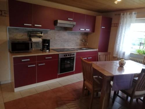 cocina con armarios rojos y mesa de madera con comedor en Ferienwohnung Altmaier - Ferien auf dem Lande, en Griebelschied