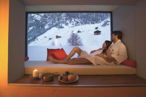 a man and woman sitting on a couch in front of a window at Hotel Rovanada Wellness & BergNatur in Vals