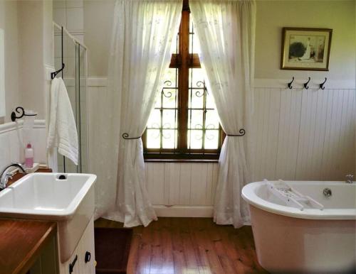 een badkamer met een bad, een wastafel en een raam bij Cedarwood Guest House in Howick