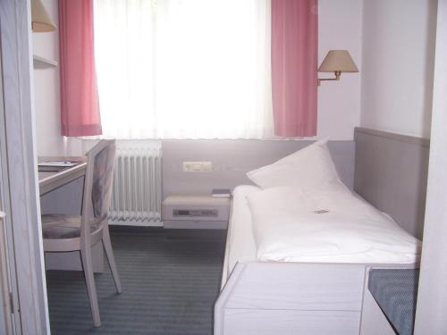 Habitación pequeña con cama, escritorio y ventana. en Hotel Zimmermann en Filderstadt