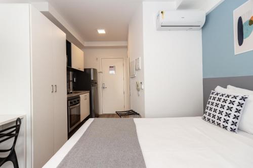 a bedroom with a white bed and a kitchen at 360 Suítes Sé in Sao Paulo
