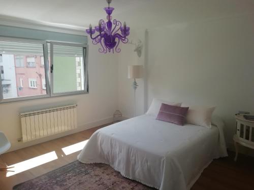 ein Schlafzimmer mit einem weißen Bett und einem Kronleuchter in der Unterkunft Céntrico y amplio piso con plaza parking in Cangas