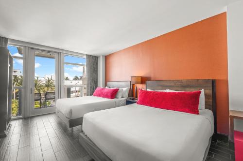 a hotel room with two beds with red pillows at The Fairwind Hotel in Miami Beach