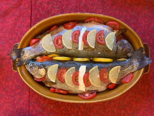 a pan of fish with slices of lemon and tomatoes at Pensiunea Deceneu in Slănic