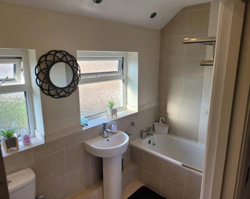 La salle de bains est pourvue d'un lavabo, d'une baignoire et d'un miroir. dans l'établissement Fabulous 3 bedroom house , sleeps up to 5-7 guest., à South Ockendon