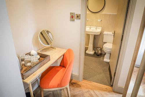 a bathroom with a vanity with a mirror and a orange chair at Hope and Anchor in Flookburgh