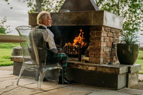 a man sitting in a chair in front of a fireplace at Newton Hall in Chathill