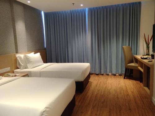 a hotel room with two beds and a desk at Hotel Excelsior Ipoh in Ipoh