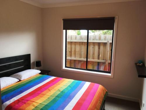 um quarto com uma cama de arco-íris e uma janela em Our Beach House em Murradoc