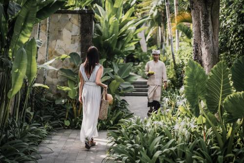 a woman in a white dress walking through a garden at The Retreat at Kharista by Ekosistem in Canggu