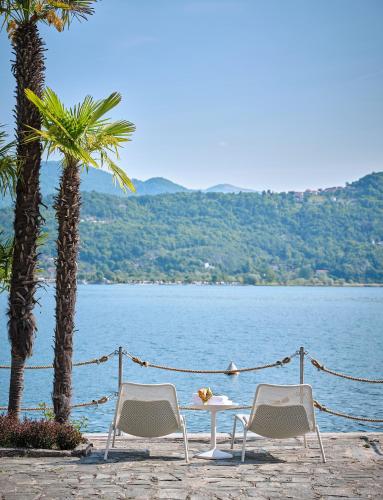 two chairs and a table and two palm trees and water at Hotel Carillon in Baveno