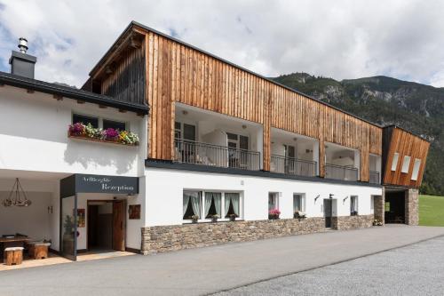 ein großes weißes Gebäude mit einem Holzdach in der Unterkunft ArlBerglife Ferienresort in Pettneu am Arlberg