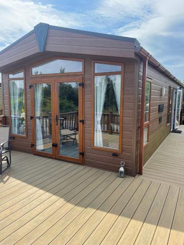 a large wooden cabin with glass doors on a deck at Fern Lodge with Hot Tub in Stonham Aspall