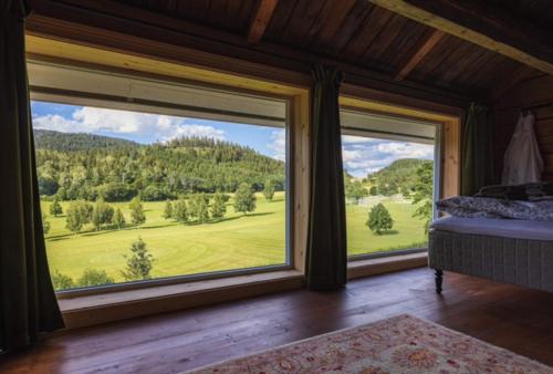 a bedroom with large windows with a view of a green field at Stokke Gård Burglamping in Stjoerdal