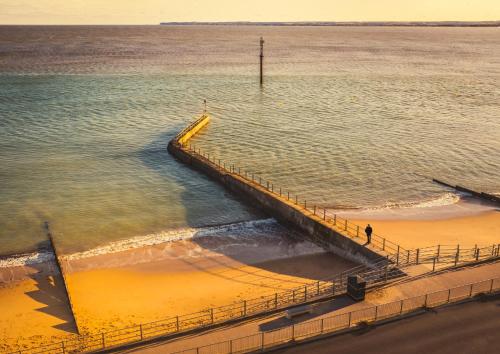 a pier in the water with a person walking on the beach at Opulent Georgian townhouse overlooking Spencer Square in Kent