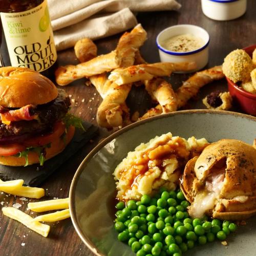 a table with a plate of food with a burger and peas at The Foresters Arms in Tarporley