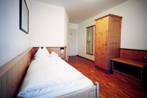 Schlafzimmer mit einem weißen Bett und einem Holzschrank in der Unterkunft Grüner Baum Garni in Krumbach