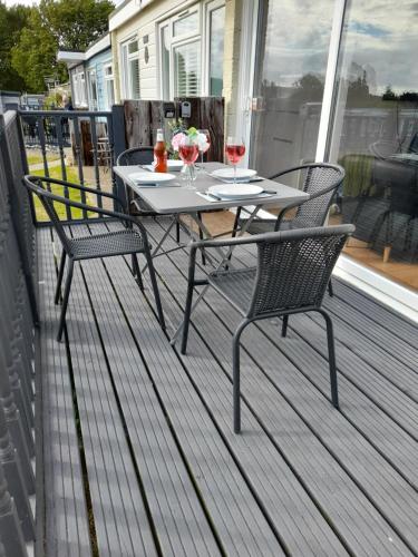 a table and two chairs on a deck with wine glasses at Sunset 128 Sandown Bay Holiday Centre Generous Ferry Saving! in Sandown
