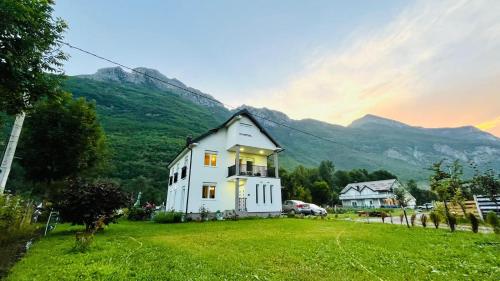 a white house in a field with mountains in the background at A Breath of Fresh Air in Gusinje