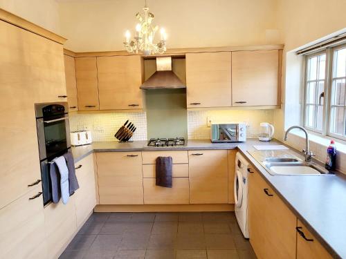 een keuken met houten kasten, een wastafel en een kroonluchter bij 5 Bedroom house in great location, near stadium NN5 in Upton