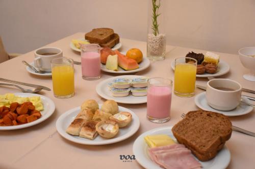 a table with plates of breakfast foods and glasses of orange juice at VOA Hotel Lancaster in Curitiba