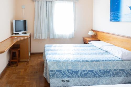 a bedroom with a bed and a desk with a television at VOA Plazza Hotel in Águas de Lindóia