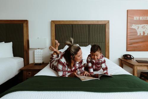 a woman and child sitting on a bed reading a book at Taos Valley Lodge in Taos
