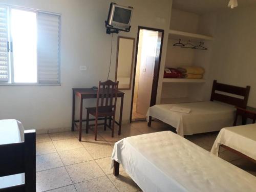 a room with two beds and a table and a tv at Pousada Moura Ávila in Dores de Campos