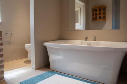 La salle de bains est pourvue d'une baignoire blanche et d'un miroir. dans l'établissement Somerset Grace Cottage, à Somerset West