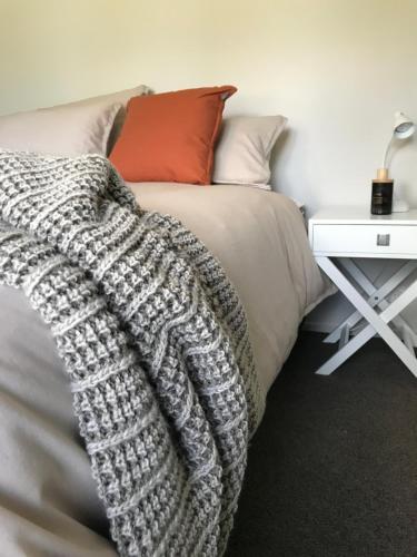a bed with a grey blanket and a white table at The Great Escape, Luxury Waterfront, HotTub in Whitianga