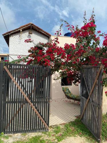 a fence with a bush of red flowers in front of a house at Chalé do Coqueiro in Luis Correia