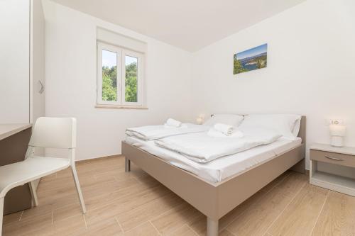 een witte slaapkamer met een bed en een stoel bij Apartments Sucic 2 in Soline