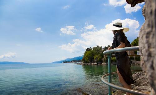 a woman in a hat standing on a railing looking at the water at Hotel Lungomare Opatija - Liburnia in Opatija