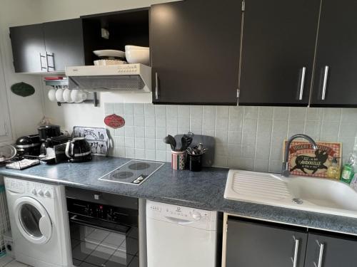 une cuisine avec des placards noirs, un lave-linge et un évier dans l'établissement Appartement 2 pièces avec balcon, ascenseur, cuisine équipée - Cabourg - FR-1-487-340, à Cabourg