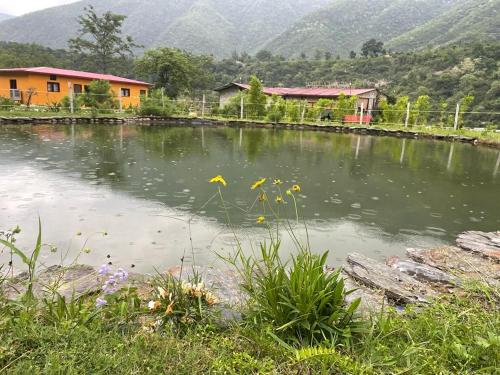 a pond of water with houses and mountains in the background at Nayar Valley Retreat in Lansdowne