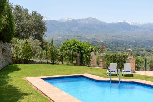 a swimming pool with two chairs and mountains in the background at Villa Elia by PosarelliVillas in Vryses
