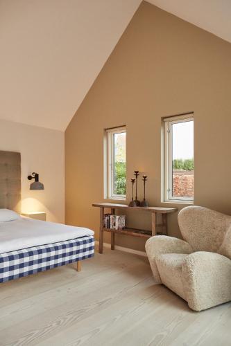 a bedroom with a bed and a chair and two windows at Gilleleje Badehotel in Gilleleje