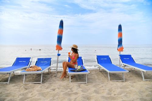 a woman sitting on a beach with chairs and umbrellas at Fortuna Beach - Seaside Hotel & SPA in Ischia