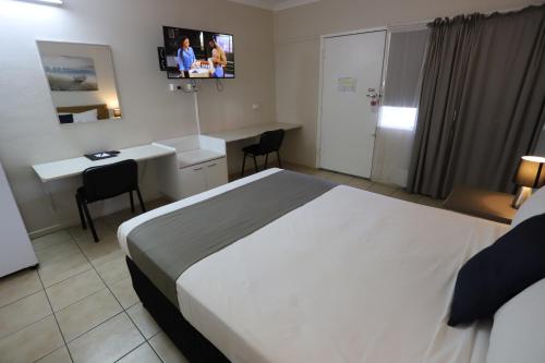 a hotel room with a bed and a desk and a tv at Tropic Coast Motel in Mackay